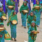 Women in vibrant attire participate in a traditional ceremony, holding wooden bowls.