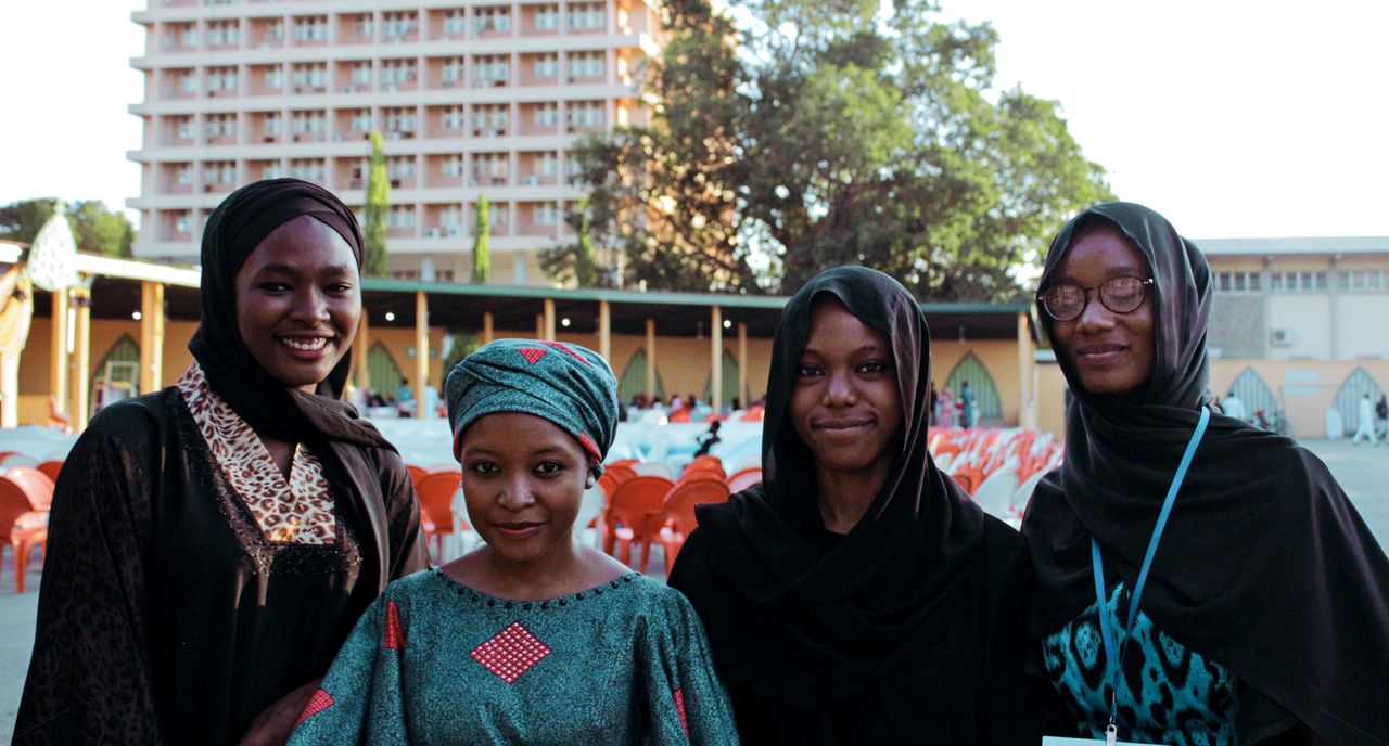 Four women smiling in traditional attire, enjoying time together outdoors near a university campus.