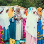 A diverse group of Muslim women praying together outdoors in vibrant traditional clothing.