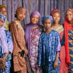 A vibrant group portrait of women wearing colorful traditional African clothing indoors.