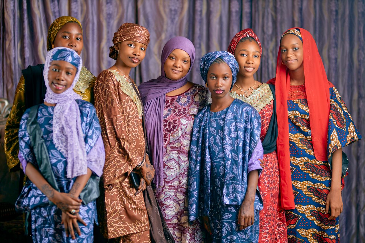 A vibrant group portrait of women wearing colorful traditional African clothing indoors.